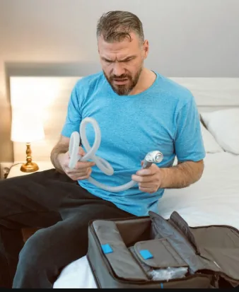Man unpacking a CPAP machine and hose from a travel bag on a bed