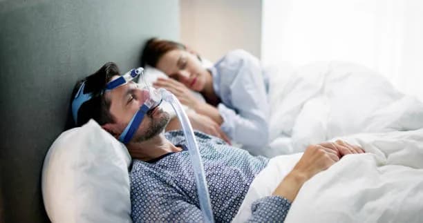 A person using a CPAP mask while resting beside their partner