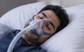A person asleep wearing a CPAP mask connected to tubing